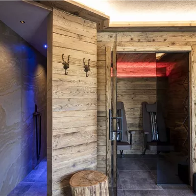 A modern wellness area with wood-paneled walls and soft lighting elements. On the right side, there are towels and fitness equipment.