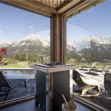 An elegant room with a view of the mountains. Outside, there is a pool and comfortable loungers.