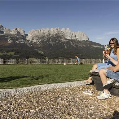 A couple relaxes on a lounger with a view of the mountains. They enjoy drinks in a picturesque setting.