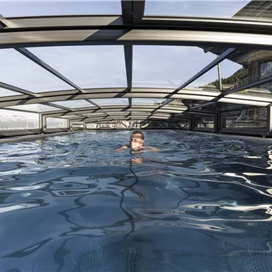 A modern pool under a glass roof with clear water. A person swims relaxed in it.