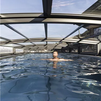 A man swims in an indoor swimming pool. The water is clear and reflects the light of the surroundings.
