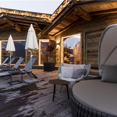 A cozy outdoor area with modern loungers and umbrellas. The wooden cladding and warm lights create a relaxed atmosphere.