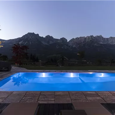 An elegant pool with blue water in front of majestic mountains. The evening atmosphere creates a relaxing ambiance.
