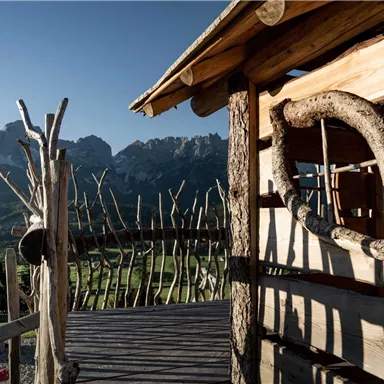 A wooden house with a rustic porch and picturesque mountain views. The clear sky and natural surroundings create a peaceful atmosphere.