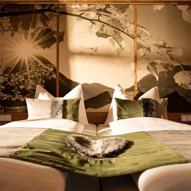 A cozy bedroom with two beds and stylish pillows. The wall is decorated with a beautiful landscape graphic that captures a lot of light.