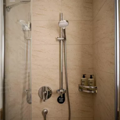 A modern shower with stainless steel fixtures and a clear glass wall. The walls are in neutral colors, and there are shampoo and shower gel dispensers.