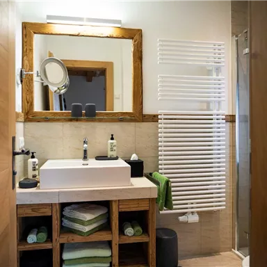 A modern bathroom with wood and tile elements. There is a sink on a wooden cabinet and decorative towels in various colors.