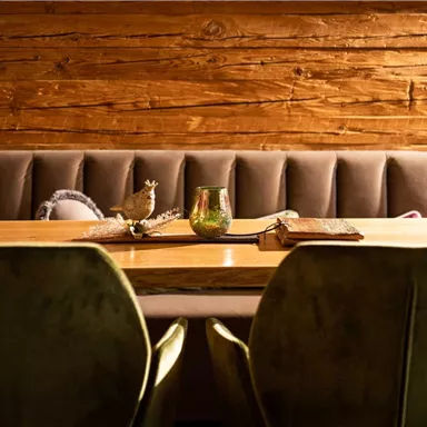 An elegant wooden dining table with two green chairs. The warm wood paneling in the background creates a cozy atmosphere.