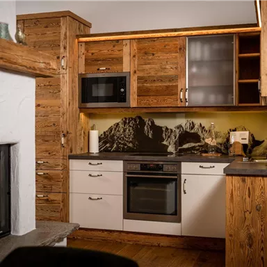 A cozy kitchen with wooden cabinets and modern appliances. The fireplace and the mountain landscape in the background create an inviting atmosphere.