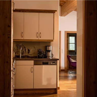 A modern kitchen with bright cabinets and a wooden floor. In the background, a cozy living area can be seen.