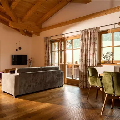 A modern living room with a wooden ceiling and large windows. There is a cozy seating area and a dining table with chairs.