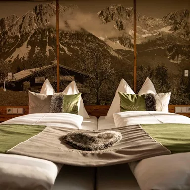 A cozy double room with two beds and a modern, rustic decor. Beautiful mountains can be seen in the background.