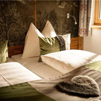 A cozy bedroom with two beds and decorative pillows. The room has plenty of natural light and a calm atmosphere.