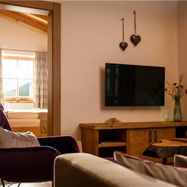 A cozy living room with a modern television and comfortable seating. The room has large windows that let in natural light, and an inviting decoration.