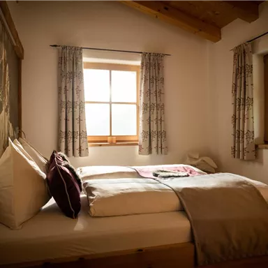 A cozy bedroom with a large bed and wooden details. Natural light comes into the room through the windows.