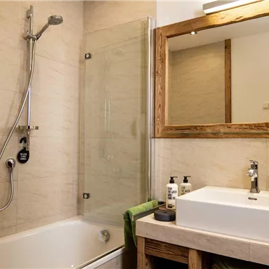 A modern bathroom with a bathtub and a shower. The wash area is elegantly designed with a large mirror and toiletries.