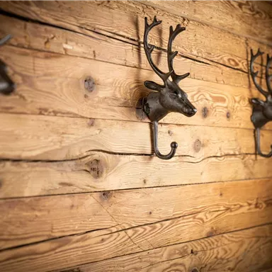 A rustic wooden wall with several metal deer heads. These serve as decorative coat hooks.