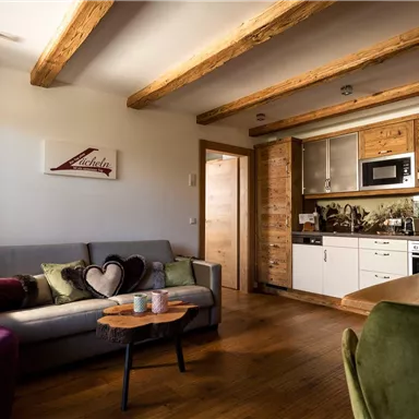 A cozy living room with wooden beams and modern furniture. The kitchen is well-equipped and bright.