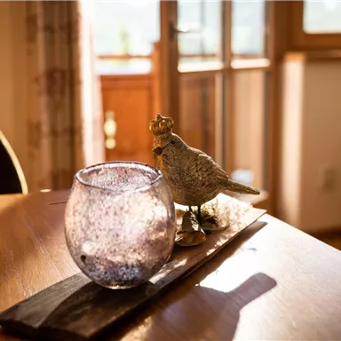 A stylish interior with a glass element and a decorative bird figure on a table. The room is brightly lit and conveys a cozy atmosphere.