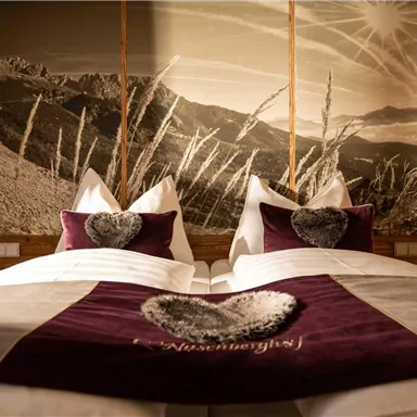 A stylish bedroom with two beds and soft pillows. The back wall features a mountainous landscape motif that creates a cozy atmosphere.