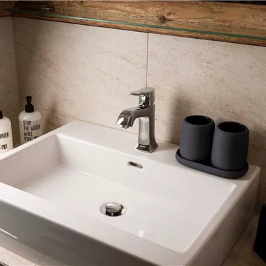 A modern sink with an elegant faucet. Care products and two cups are placed next to it.