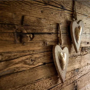 Two wooden hearts hang on a rustic wooden wall. The hearts have a shiny interior and add a warm, charming touch to the space.