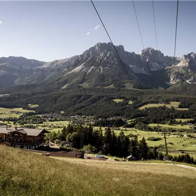 A breathtaking mountain landscape with green meadows and majestic peaks. In the foreground stands a building, surrounded by nature.