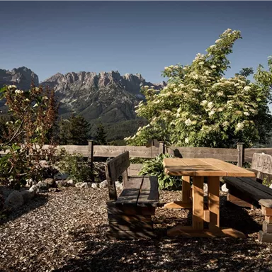 A cozy seating area made of wood in a natural setting. In the background, majestic mountains and trees can be seen.
