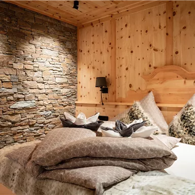 A cozy bedroom with wood paneling and a stone wall. The bed is decorated with soft pillows and blankets.