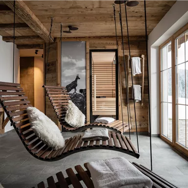 A stylish relaxation room with hanging wooden loungers and cozy cushions. Large windows offer a view of the snow-covered landscape.