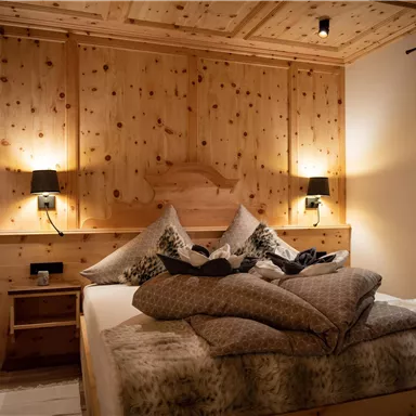A cozy bedroom with wooden walls and a large bed. Soft lighting and a calm atmosphere create an inviting space.