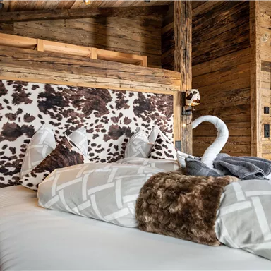 A cozy bedroom with a rustic wood design. The bed has a striking headboard with a cowhide look and is adorned with soft pillows.