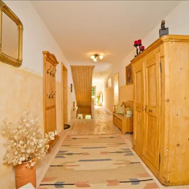 Ein heller und einladender Flur mit Holzmöbeln und einem Teppich. Die Wände sind sanft beige gestrichen und es gibt Pflanzen und Dekorationen.