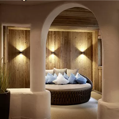 A stylish room with a round couch and blue cushions. The walls are made of wood and softly illuminated.