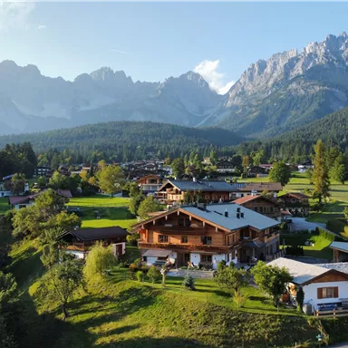 Eine malerische Berglandschaft mit grünen Wiesen und traditionellen chalets. Im Hintergrund sind majestätische Berge zu sehen.