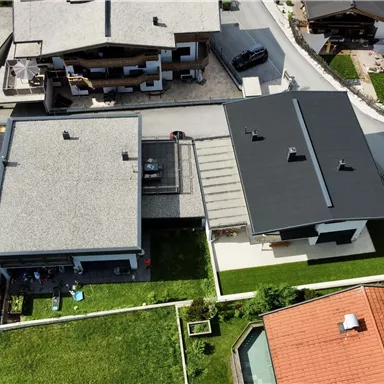 Ein Luftbild von modernen Häusern in einer ruhigen Wohngegend. Die Gebäude sind von Grünflächen umgeben und haben unterschiedliche Dachfarben.