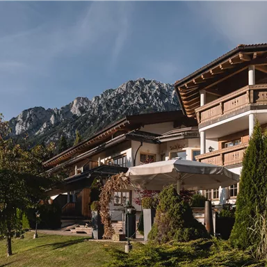 Ein charmantes Gebäude mit traditioneller Architektur inmitten einer malerischen Landschaft. Im Hintergrund erheben sich majestätische Berge unter einem klaren Himmel.