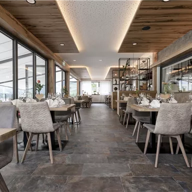 Ein modernes Restaurant mit großen Fenstern und Holzdekor. Die Tische sind elegant gedeckt und laden zum Essen ein.