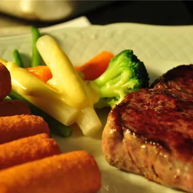 A deliciously grilled steak lies next to colorful vegetables and carrot sticks. The plate is attractively arranged and showcases a balanced meal.