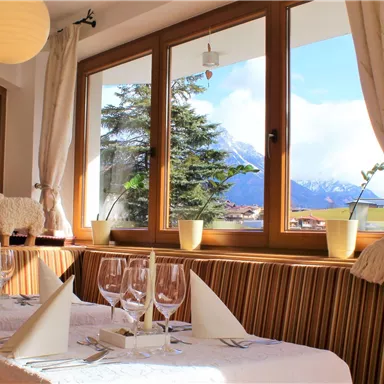 Ein einladendes Restaurant mit eleganter Tischdekoration und Blick auf die Berge. Große Fenster sorgen für viel Tageslicht und eine gemütliche Atmosphäre.