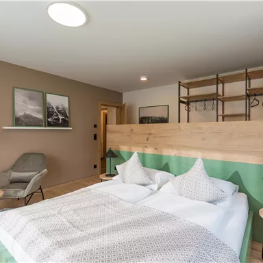 A modern bedroom with a double bed and a wood panel. The decor is minimalist and stylish with an armchair and an open wardrobe.