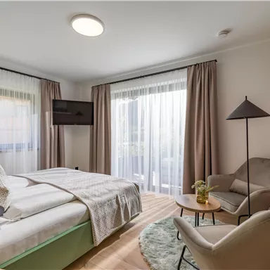 A modern bedroom with a double bed and a comfortable armchair. Large windows bring plenty of daylight into the room.