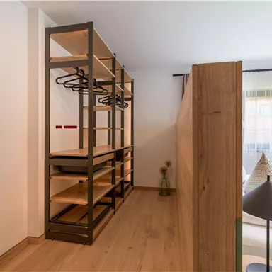 A modern room with an open wardrobe and a cozy bed. Large windows provide plenty of natural light.