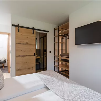 A modern bedroom with a double bed and a cozy atmosphere. The walls are partially made of wood and a television is mounted on the wall.