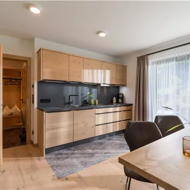 A modern kitchen with wooden cabinets and a black countertop. Large windows provide plenty of natural light.