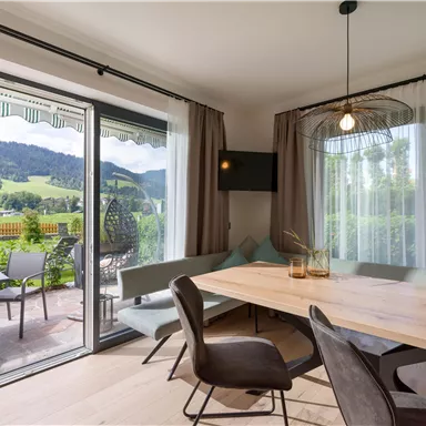 A bright and modern dining room with a large table and comfortable chairs. Through the windows, there is a beautiful view of the mountains and the landscape.