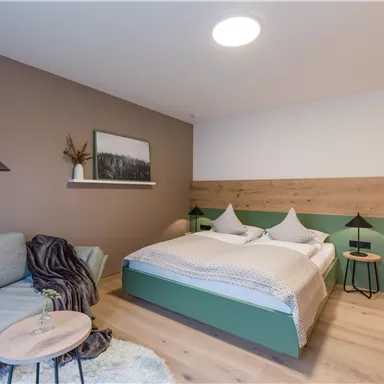 A stylish bedroom with a double bed and modern design. There is a cozy seating area with a sofa and a small table.