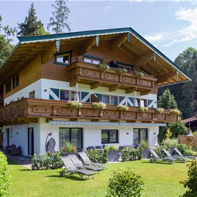 A modern Alpine house with a large garden. Loungers and plants adorn the surroundings.