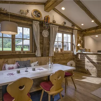 A cozy interior with wooden furniture and large windows that overlook a green landscape. The dining table is beautifully set and invites you to linger.