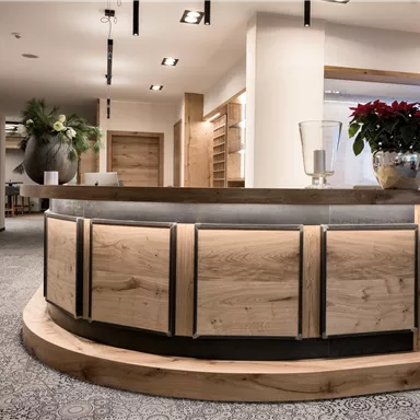 A modern reception area with a curved reception desk made of wood. On the desk, there are decorative plants and a clear, stylish atmosphere.
